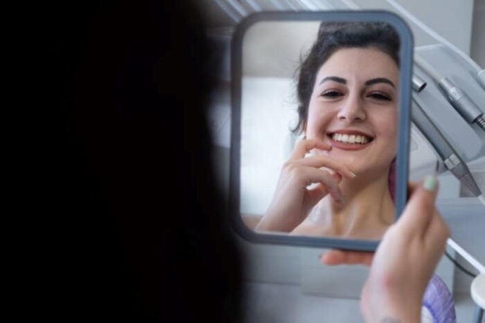 Close-up of a woman checking a loose tooth in the mirror, following safe home remedies